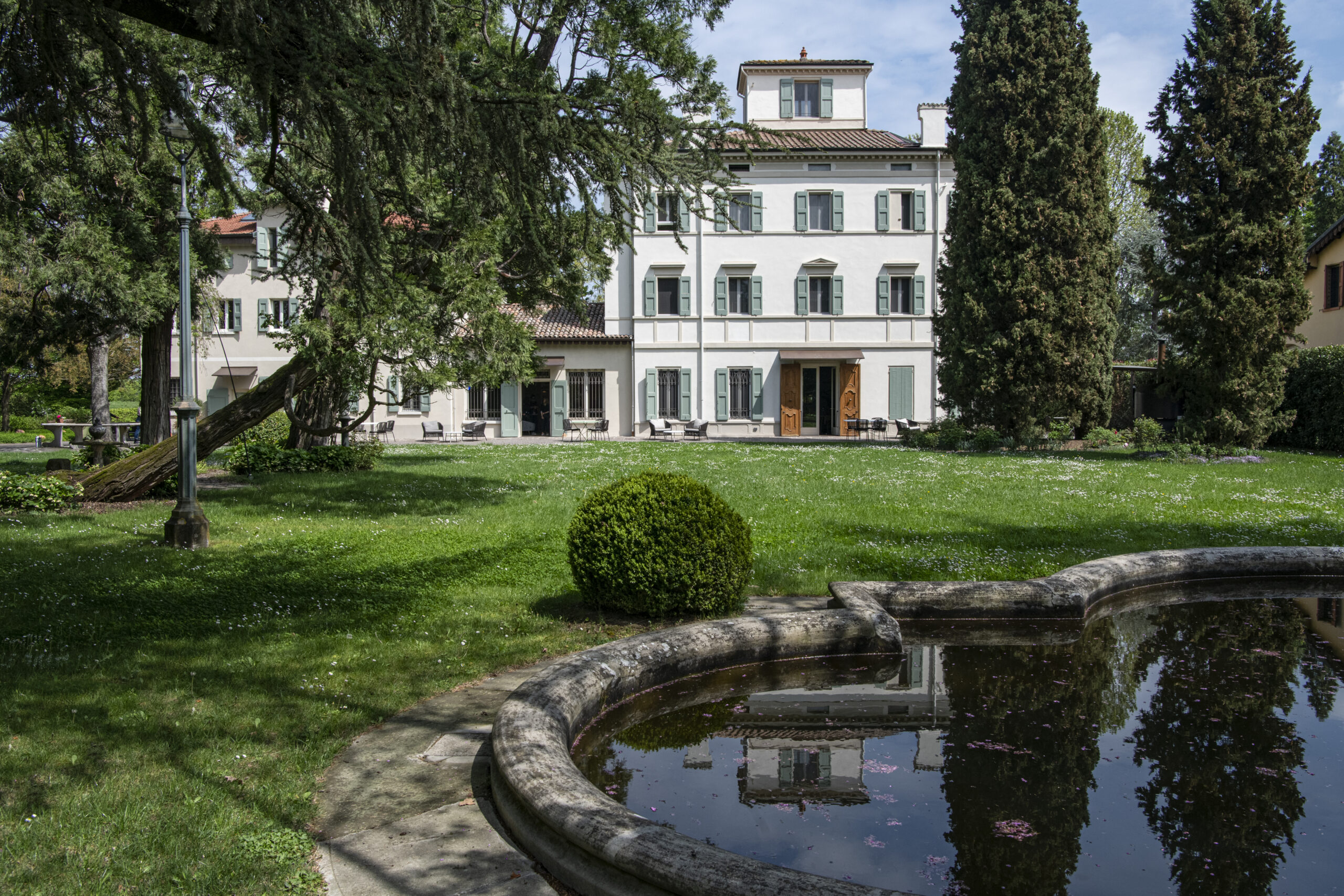 Villa storica bianca a tre piani con persiane verdi circondata da un ampio giardino e laghetto decorativo